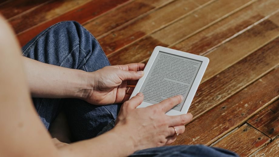 Close-up of hands holding an e-reader indoors on a wooden floor, emphasizing digital reading.