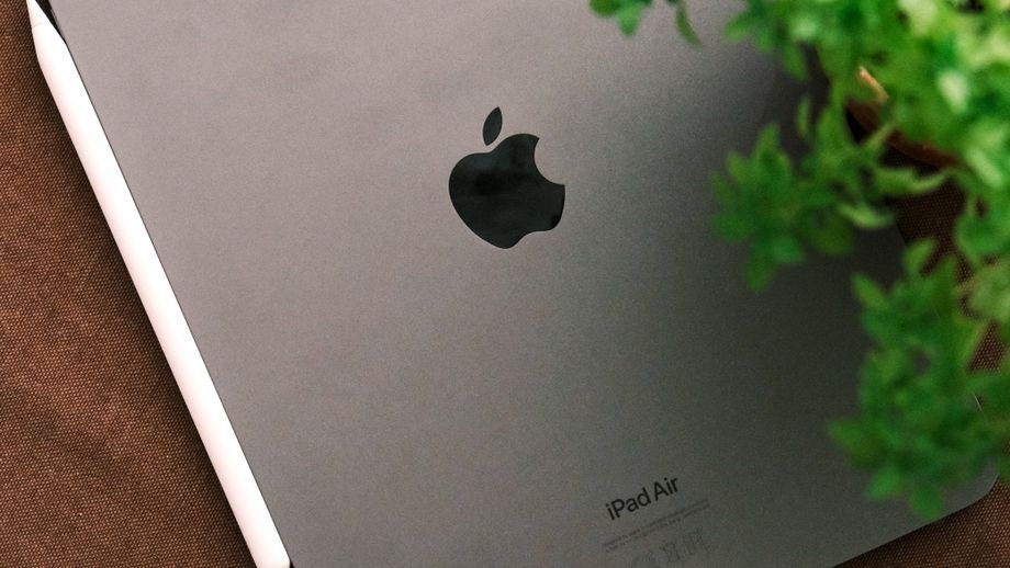 Top view of a sleek tablet and stylus on a brown surface beside a green plant.